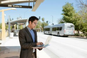 a man using a laptop while standing on the bus stop